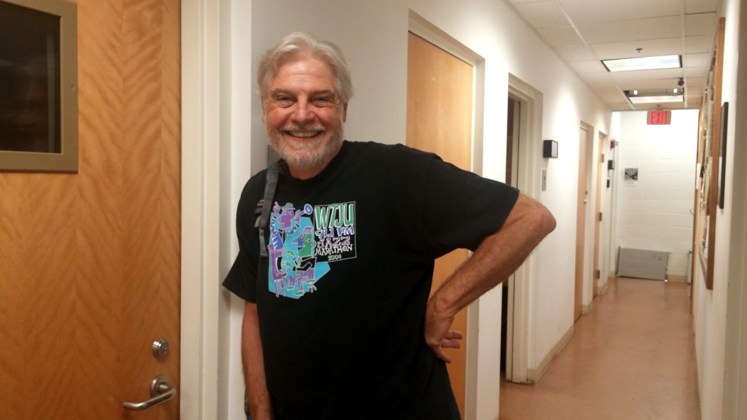 Man in black t-shirt leans against wall in long hallway